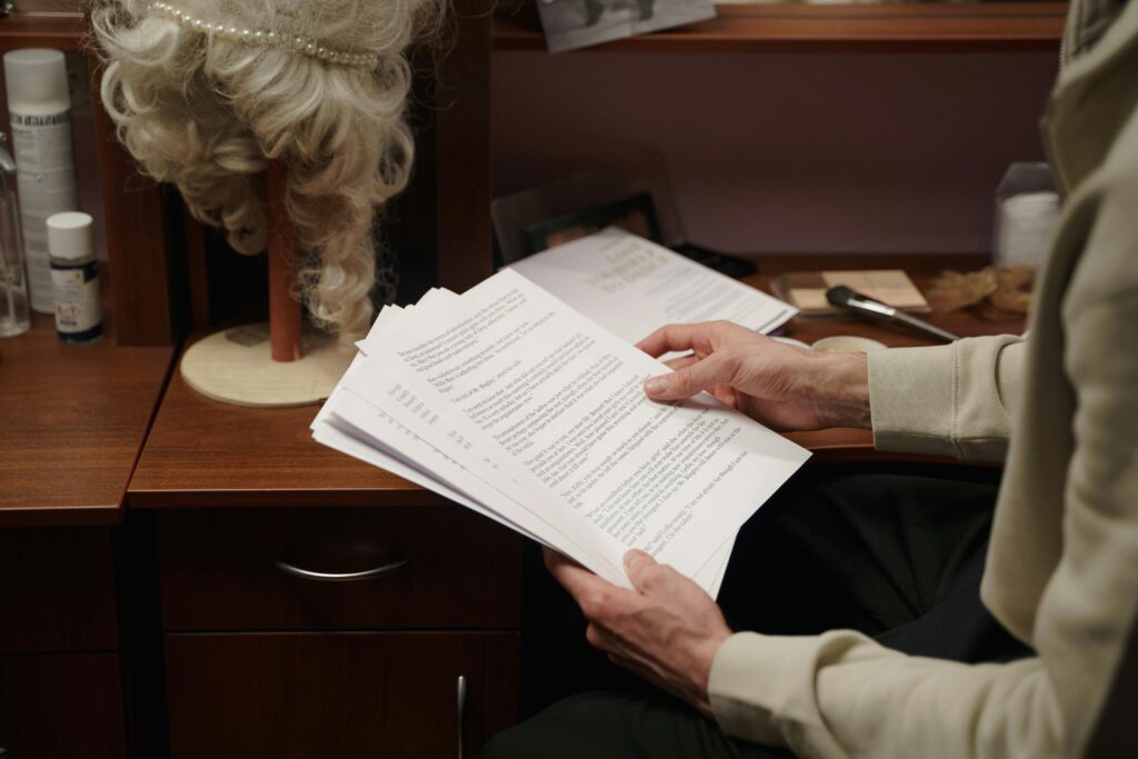 An actor reviews acting scripts in a backstage dressing room, preparing for a theater rehearsal.
