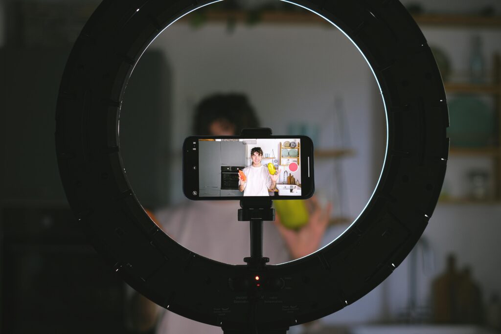 An actor records a video using a smartphone and ring light in a kitchen setting. Creating content is a cost of acting.