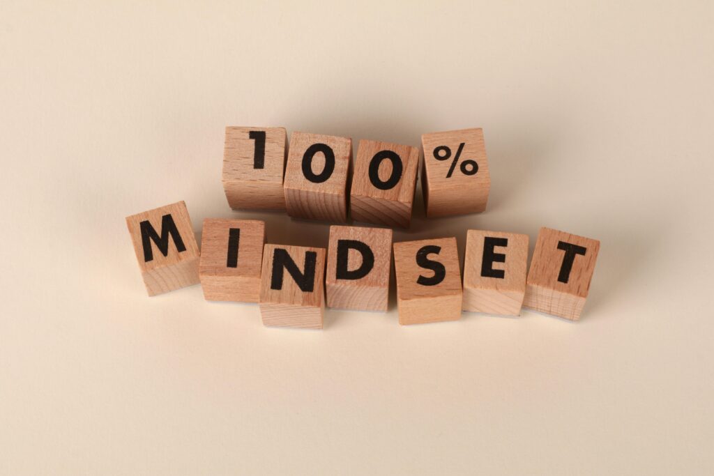Wooden blocks arranged to spell '100% Mindset' on a neutral beige background, words of wisdom promoting positivity.