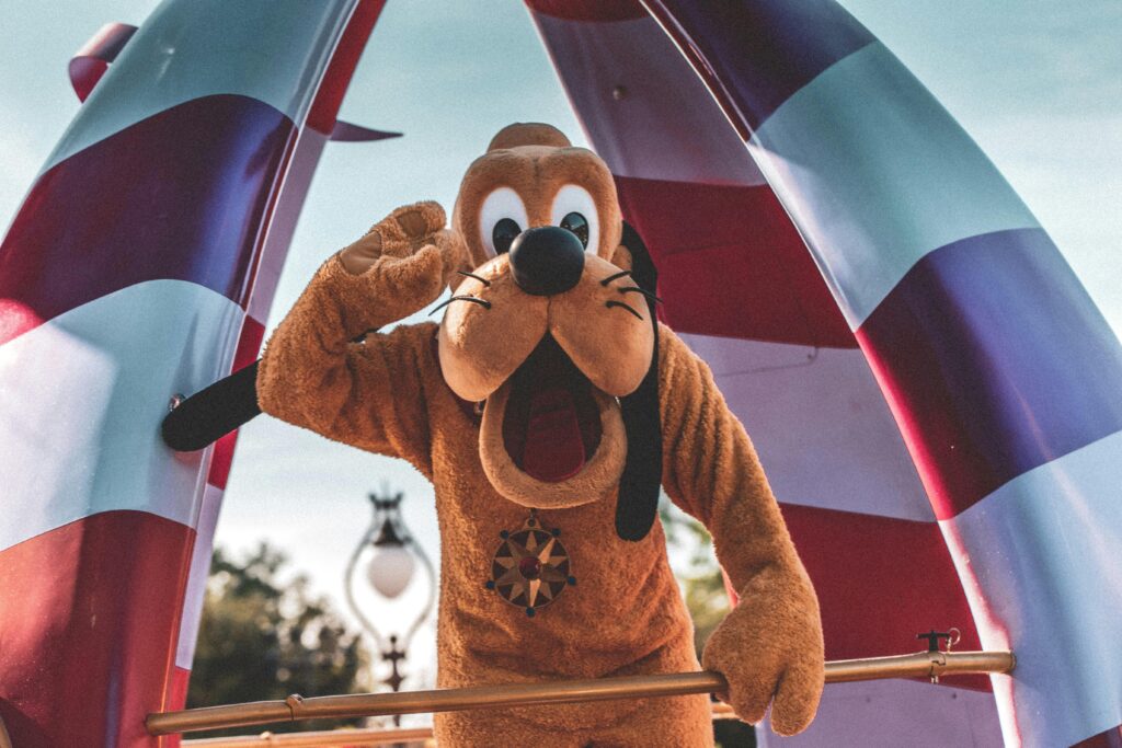 An actor performing as Playful Pluto character waving during a sunny Orlando parade at his amusement park side hustles.