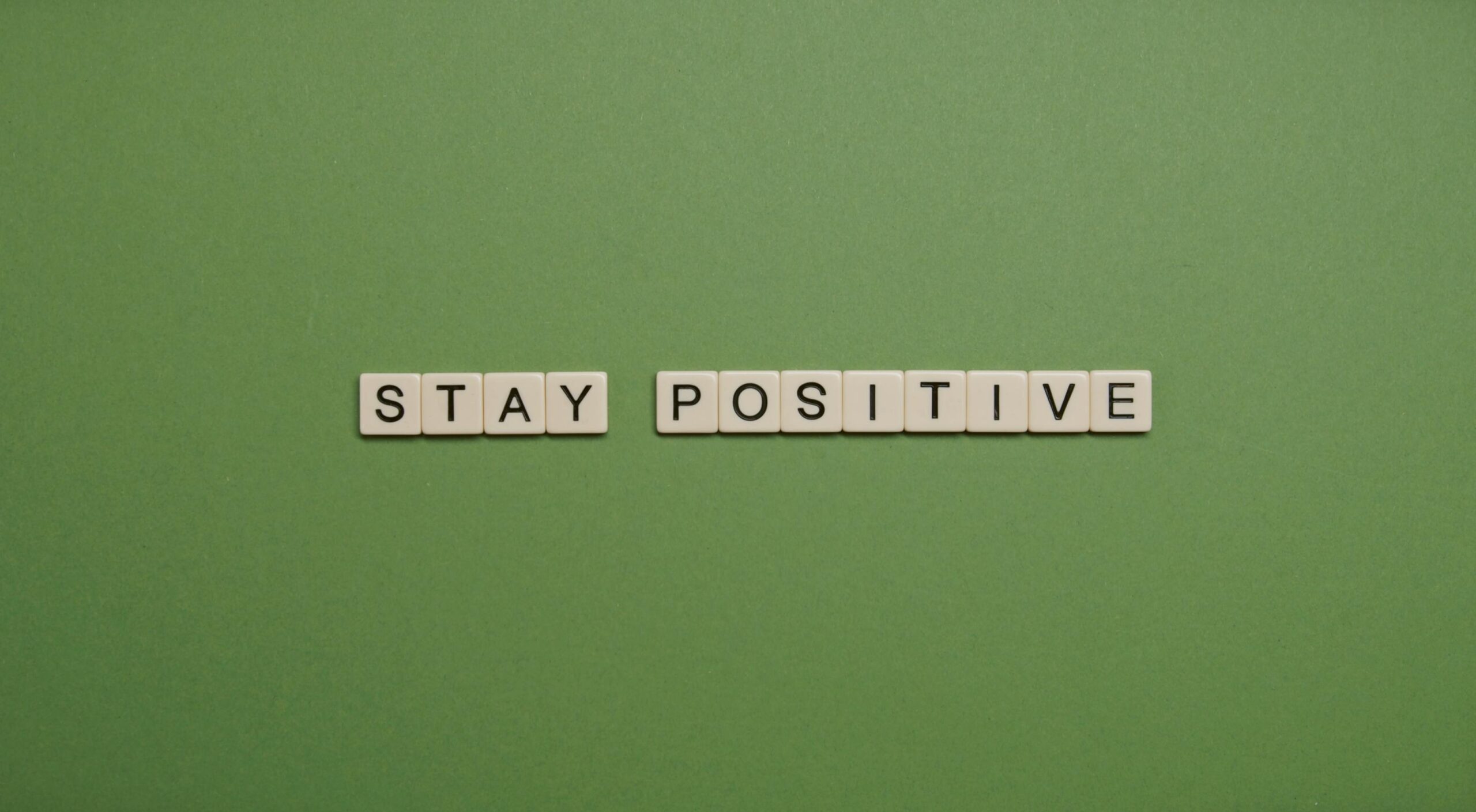 "Stay Positive" words of wisdom spelled with letter tiles on a green backdrop.