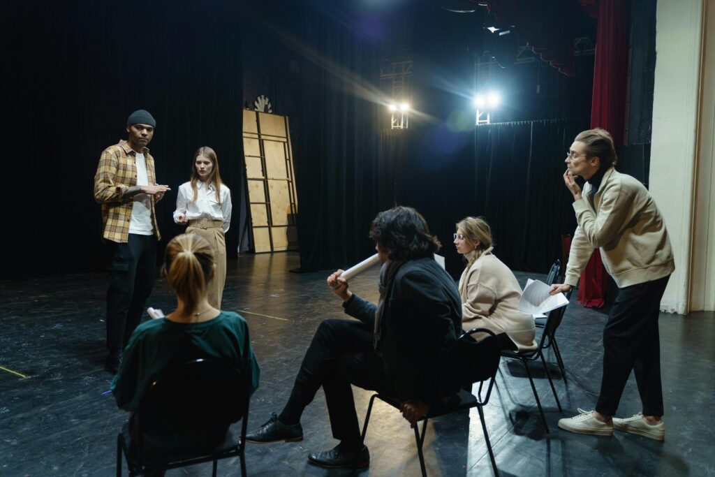 Actors rehearsing on stage with director's guidance and feedback in a theater live performance for their paid acting classes.
