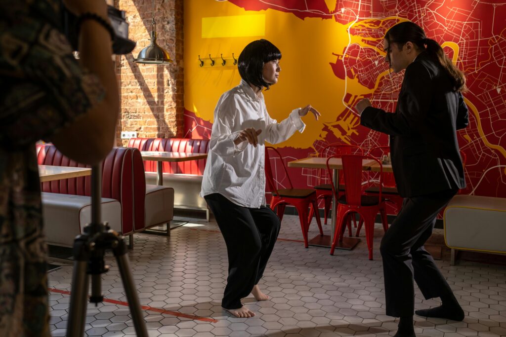 Actors rehearsing a scene in a colorful café during a film shoot as part of their paid acting classes and assignment.