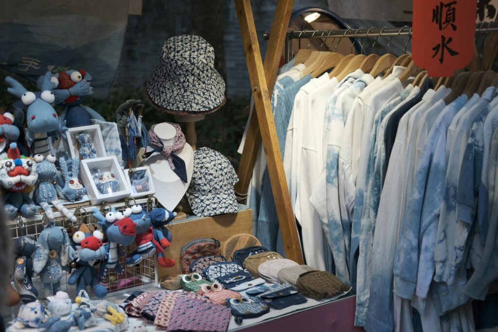 An actor sells items as their sidehustles. A vibrant flea market stall featuring handmade crafts and clothing displayed neatly.