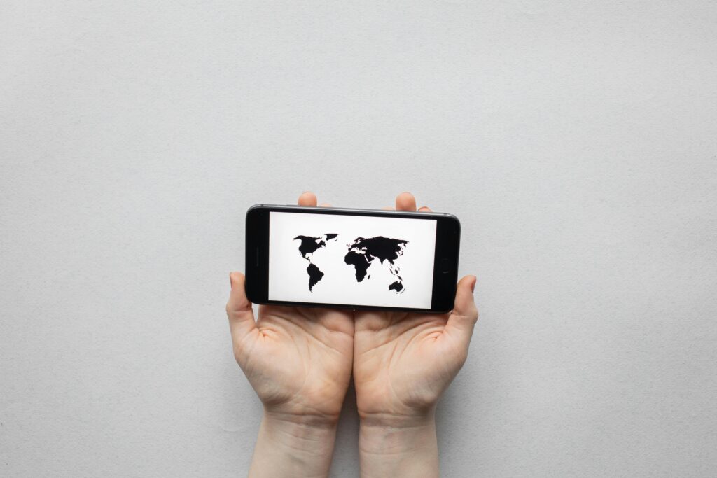 Actor searching for online and local acting classes near them in Alaska. Hands holding a smartphone displaying a world map on a white background.