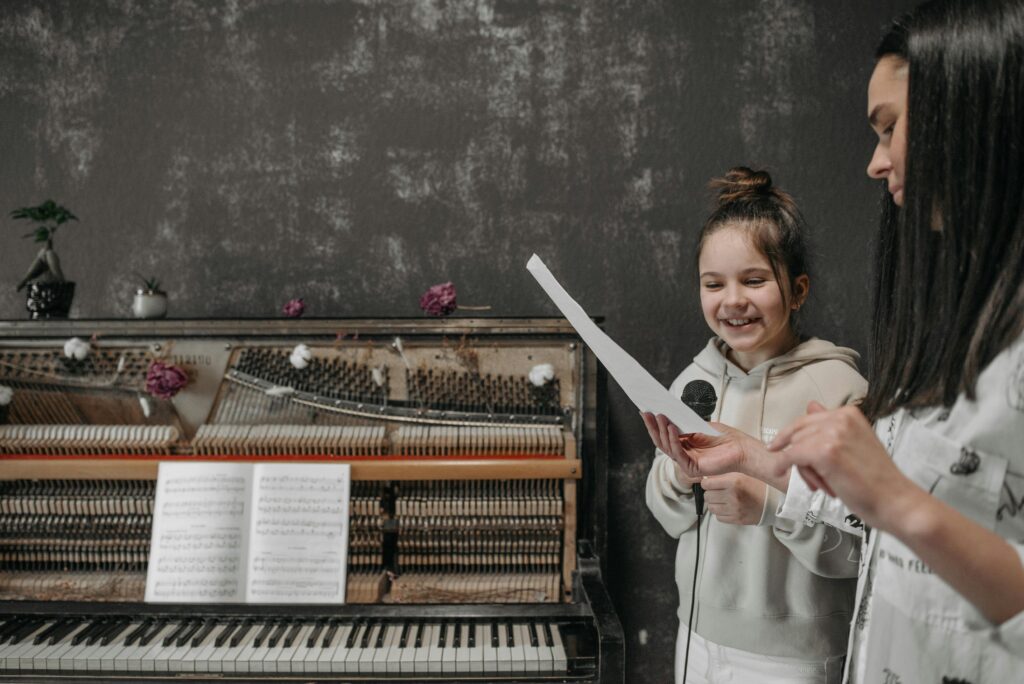 An actor teaching a young girl how to play piano as a side hustle to make money.
