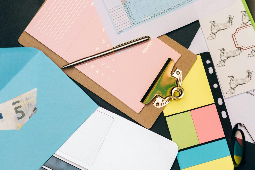 Actor organizinf and planning their side hustles to align with their goals and to create multiple streams of income. Neatly arranged desk supplies with clipboard, euro bill, and colorful notes.