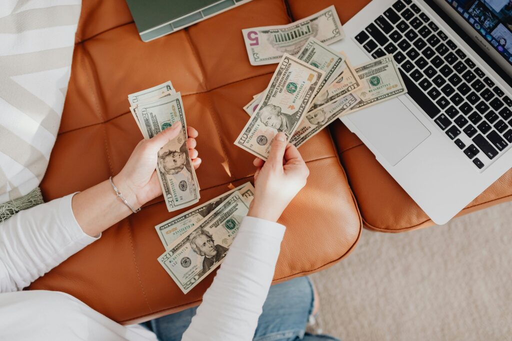 An actor counts US dollar bills on a couch with a laptop, symbolizing financial planning for their paid acting classes.
