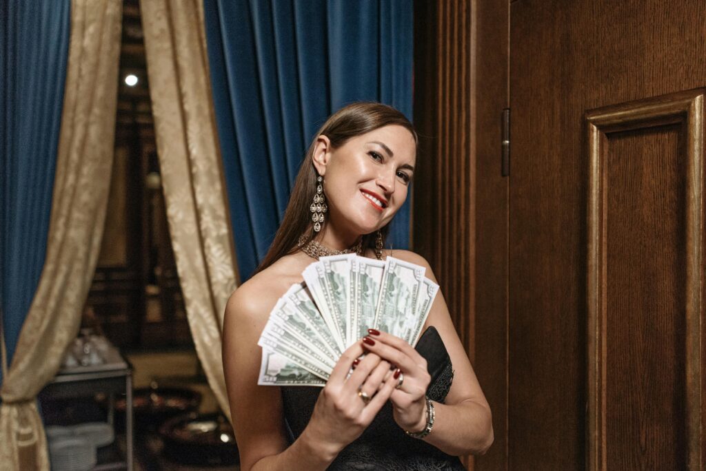 An actor in a glamorous setting holds a fan of cash from her side hustles.