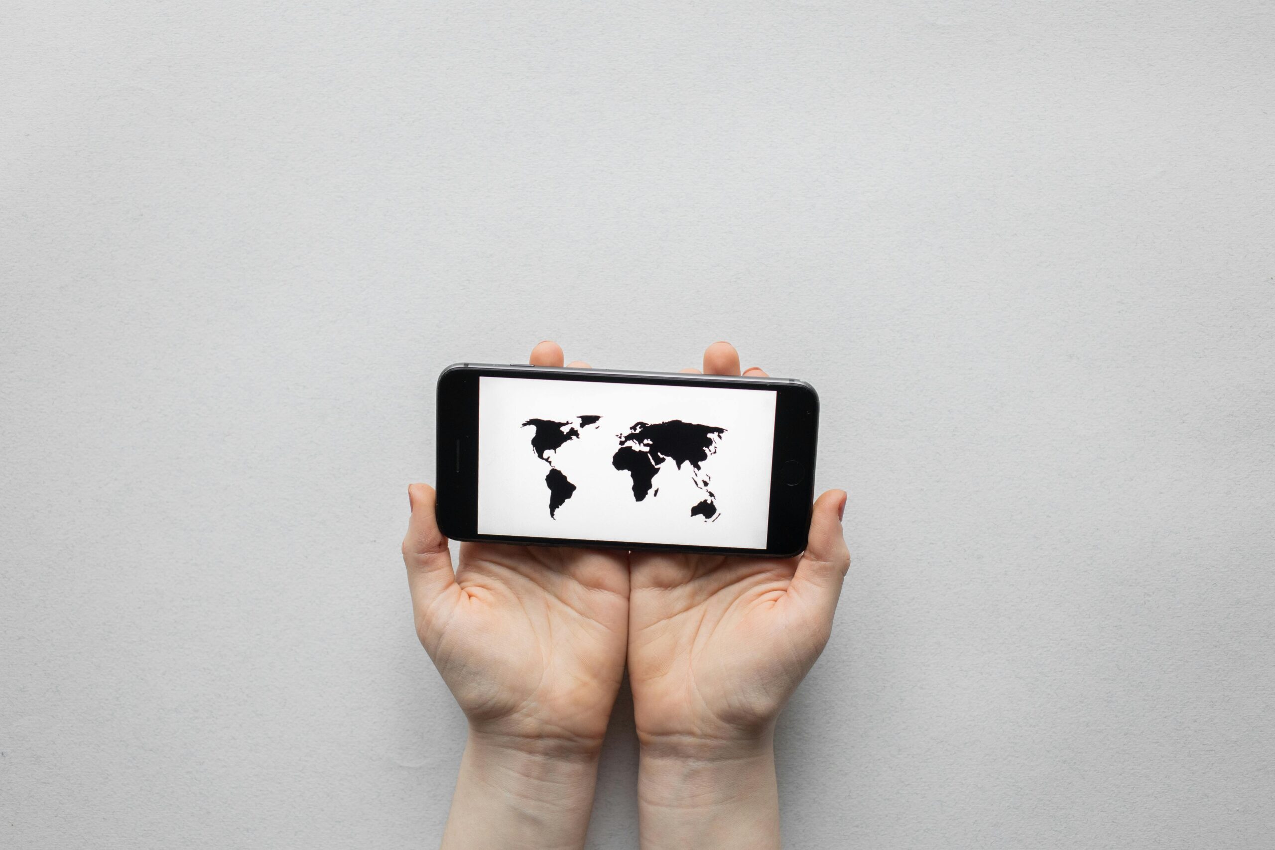 Actor searching for online and local acting classes near them in Georgia. Hands holding a smartphone displaying a world map on a white background.